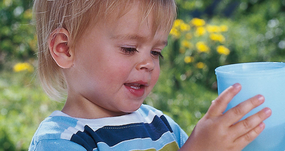 A young child is holding a blue cup outdoors.