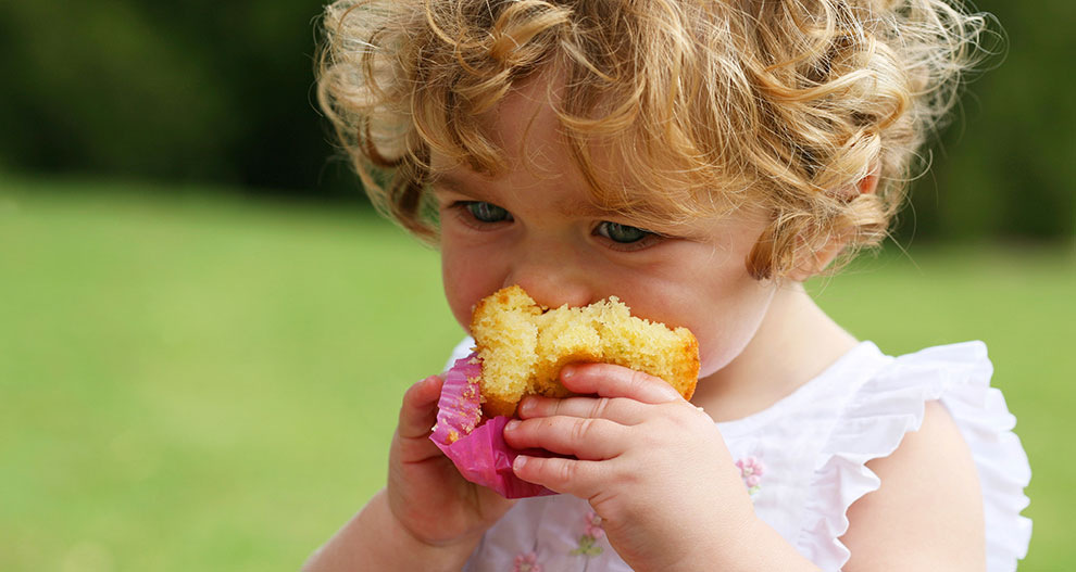 A child with curly hair is eating a yellow muffin.