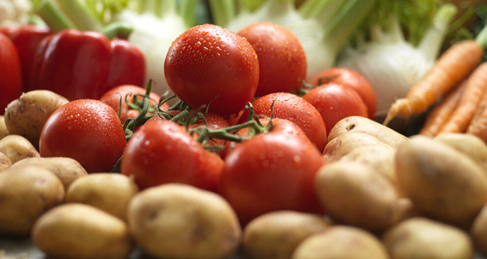 Fresh vegetables including tomatoes, carrots, potatoes, and bell peppers.